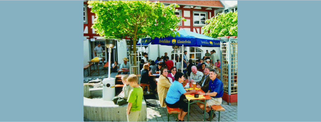 Personen an Biertischgarnitur unter einem Sonnenschirm